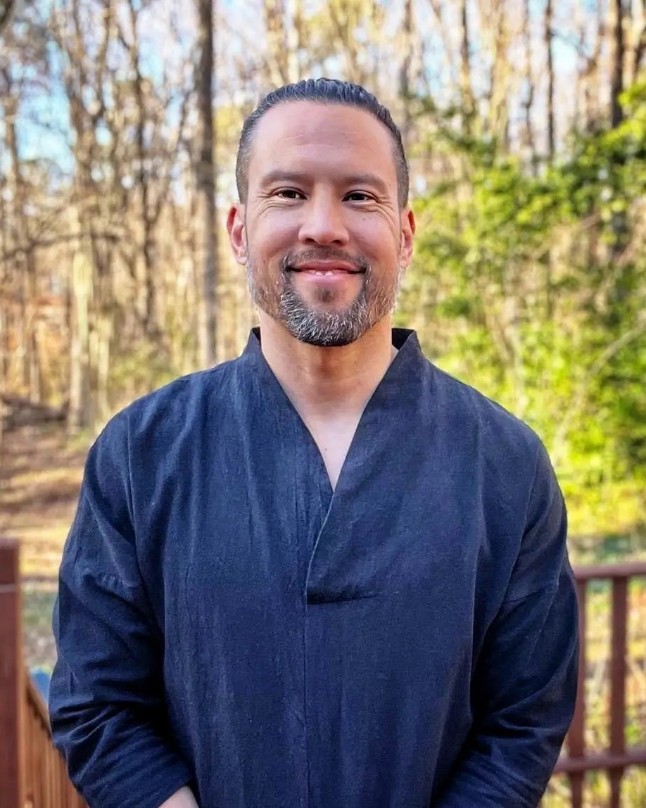 Portrait of David Beaudry, smiling, in a dark Qigong jacket outdoors