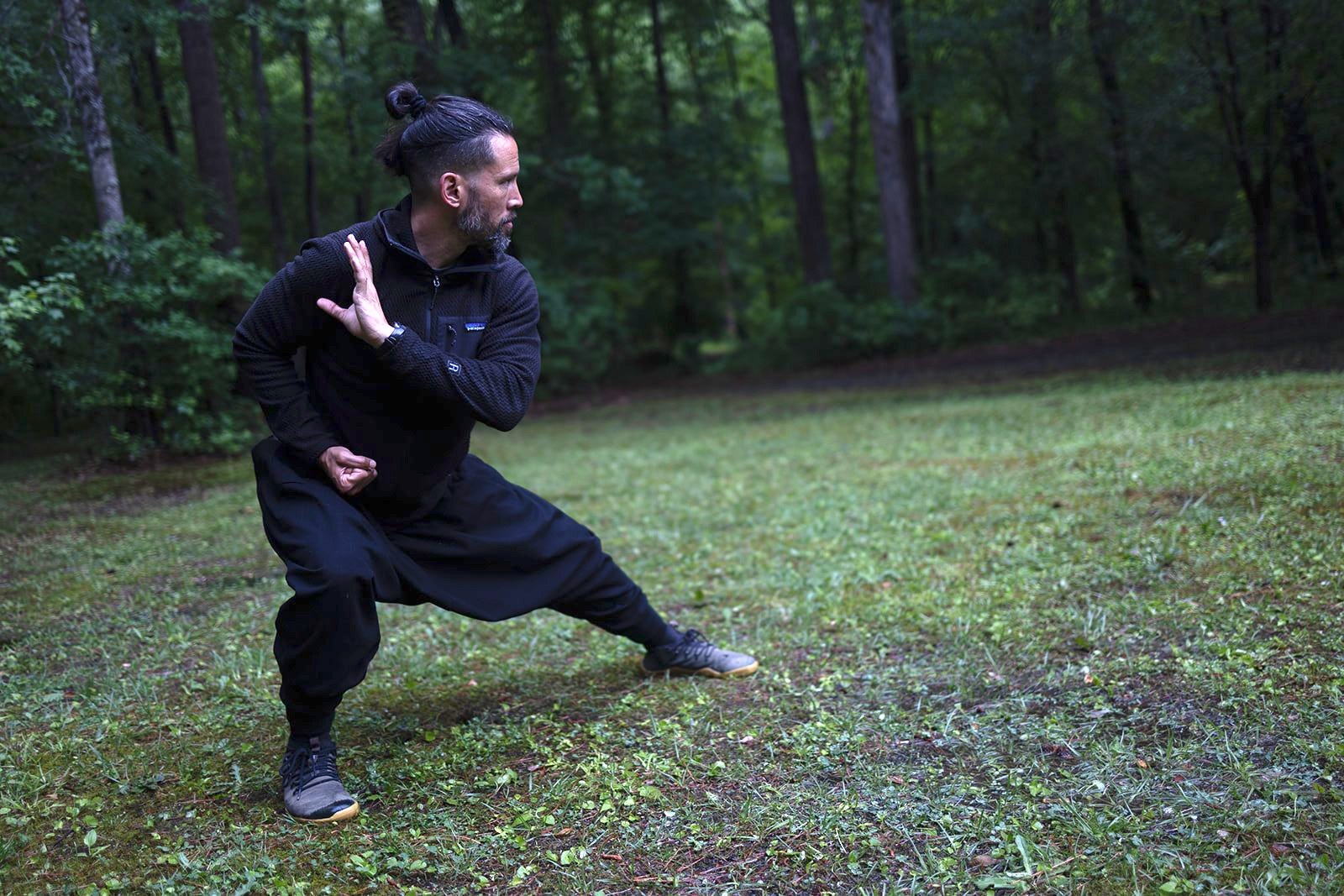 David Beaudry in black, sunk into a deep, low fighting stance in the forest